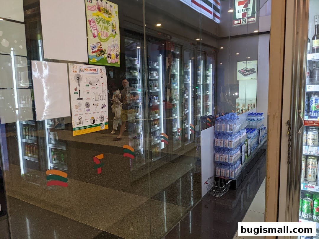 Exterior view of a 7-Eleven store with refrigerators stocked with drinks and promotional posters.