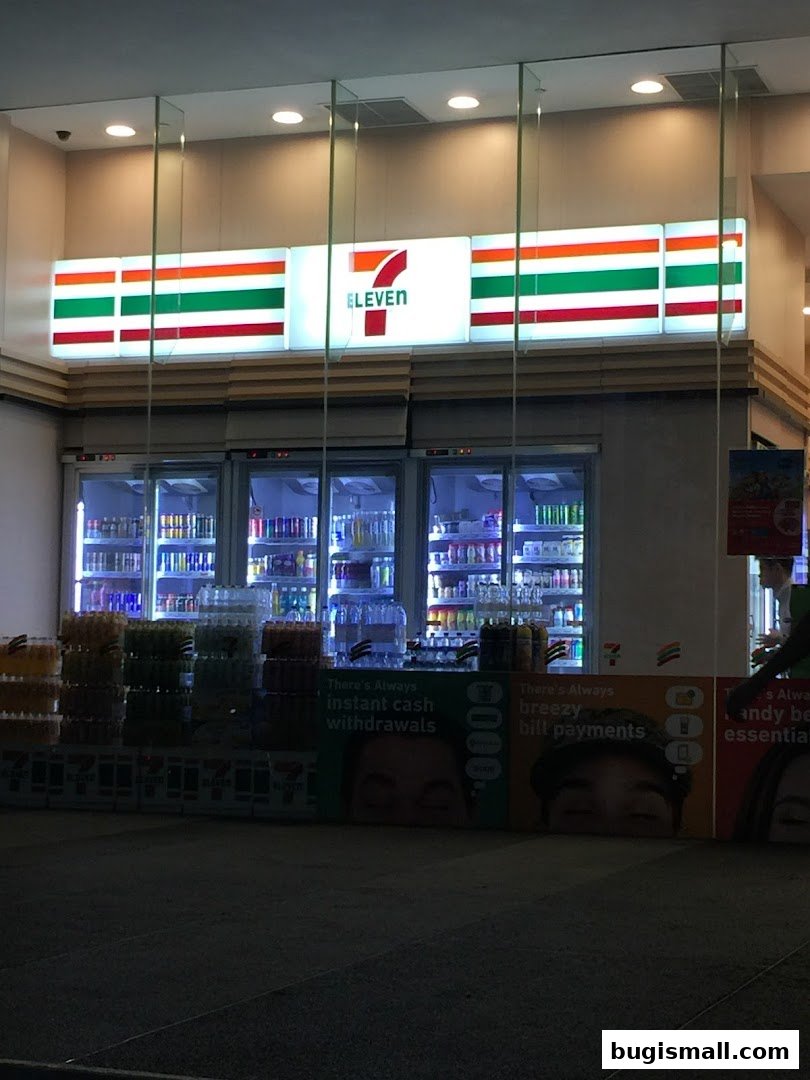 The brightly lit exterior of a 7-Eleven convenience store at night, showcasing drinks and promotional displays.