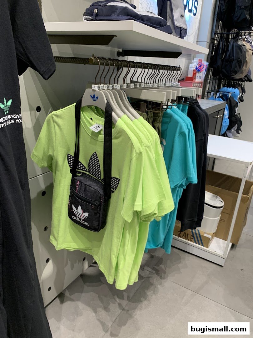 A rack of neon green Adidas t-shirts with a small black Adidas crossbody bag displayed.