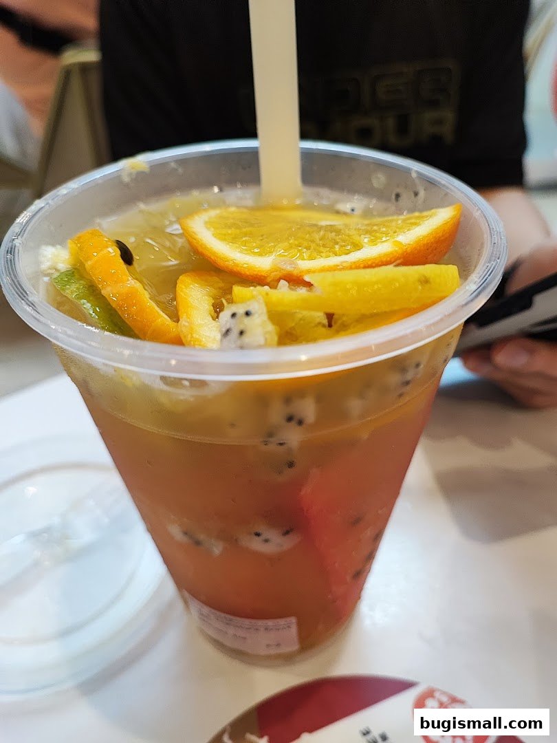 A refreshing fruit tea with orange slices, kiwi, and dragon fruit in a clear plastic cup.
