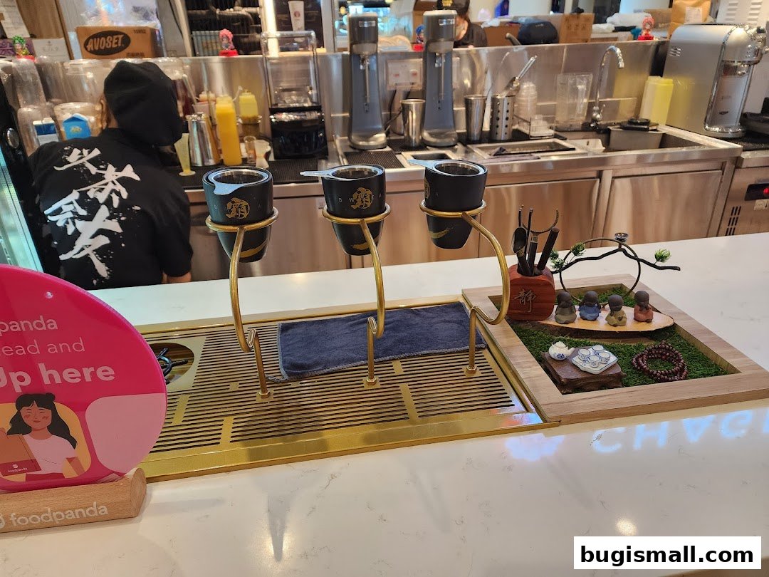 A tea shop counter with brewing equipment, decorative items, and a staff member in the background.
