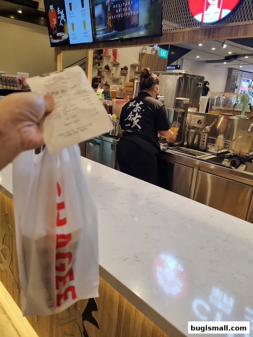 A person holds a receipt and a shopping bag in front of a tea shop counter.