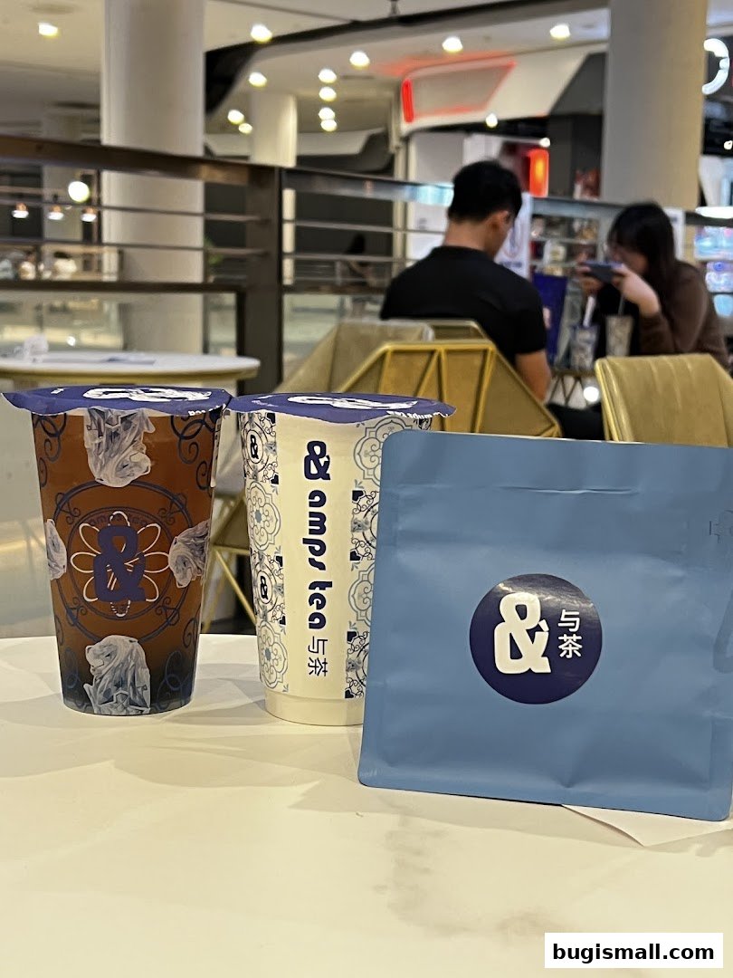 Two drinks and a blue bag from &TEA on a white table with people in the background.