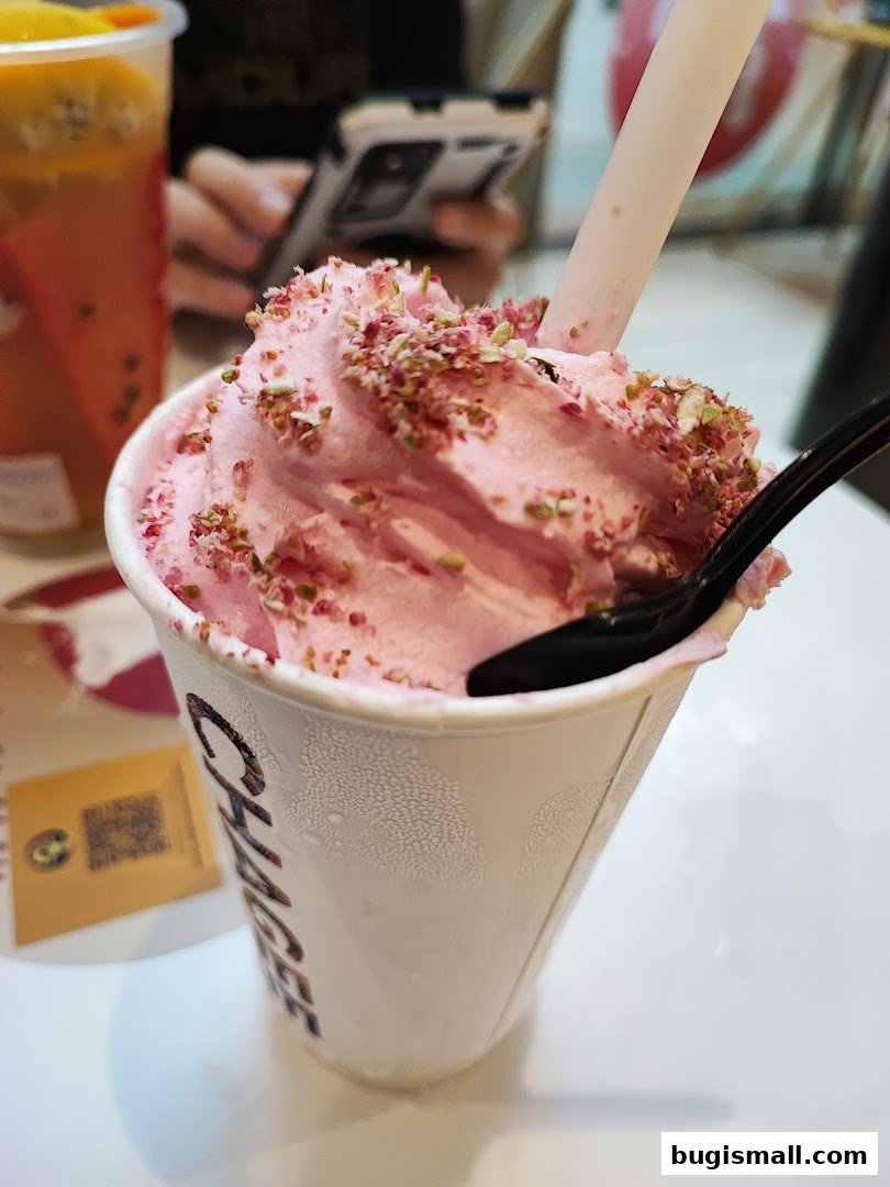 A close-up of a pink soft-serve ice cream topped with sprinkles in a white cup.
