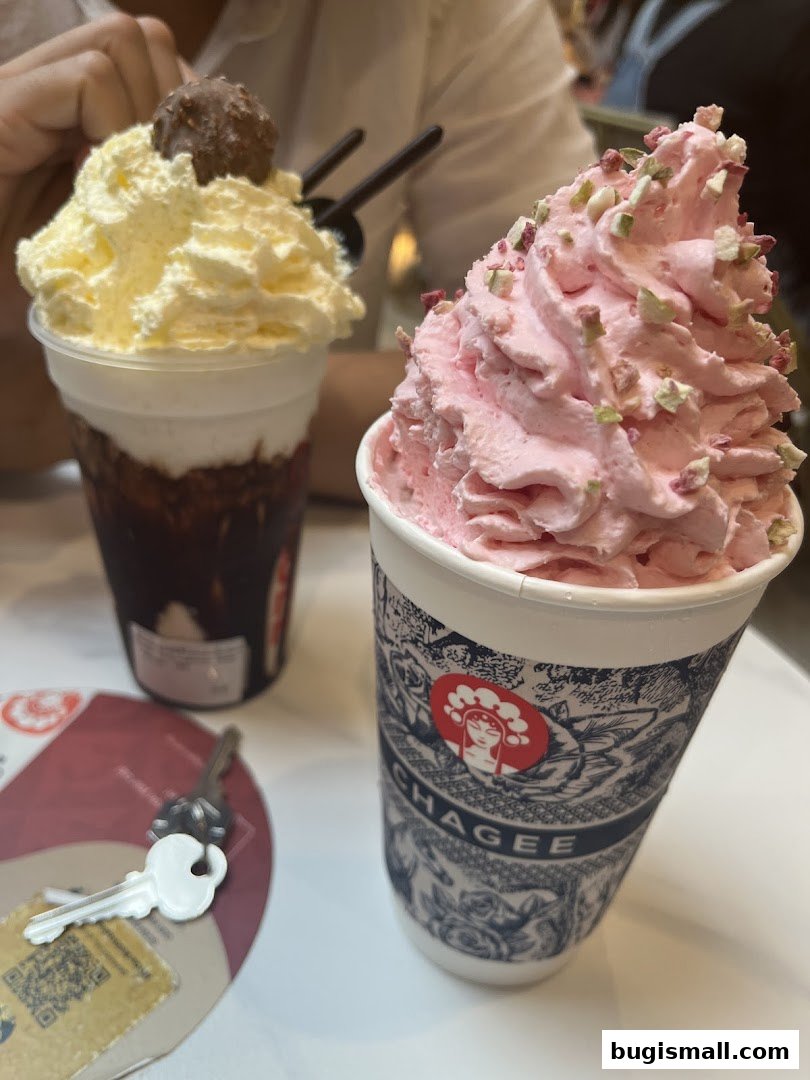 Two refreshing drinks, one with whipped cream and a chocolate ball, the other with pink cream and nuts.