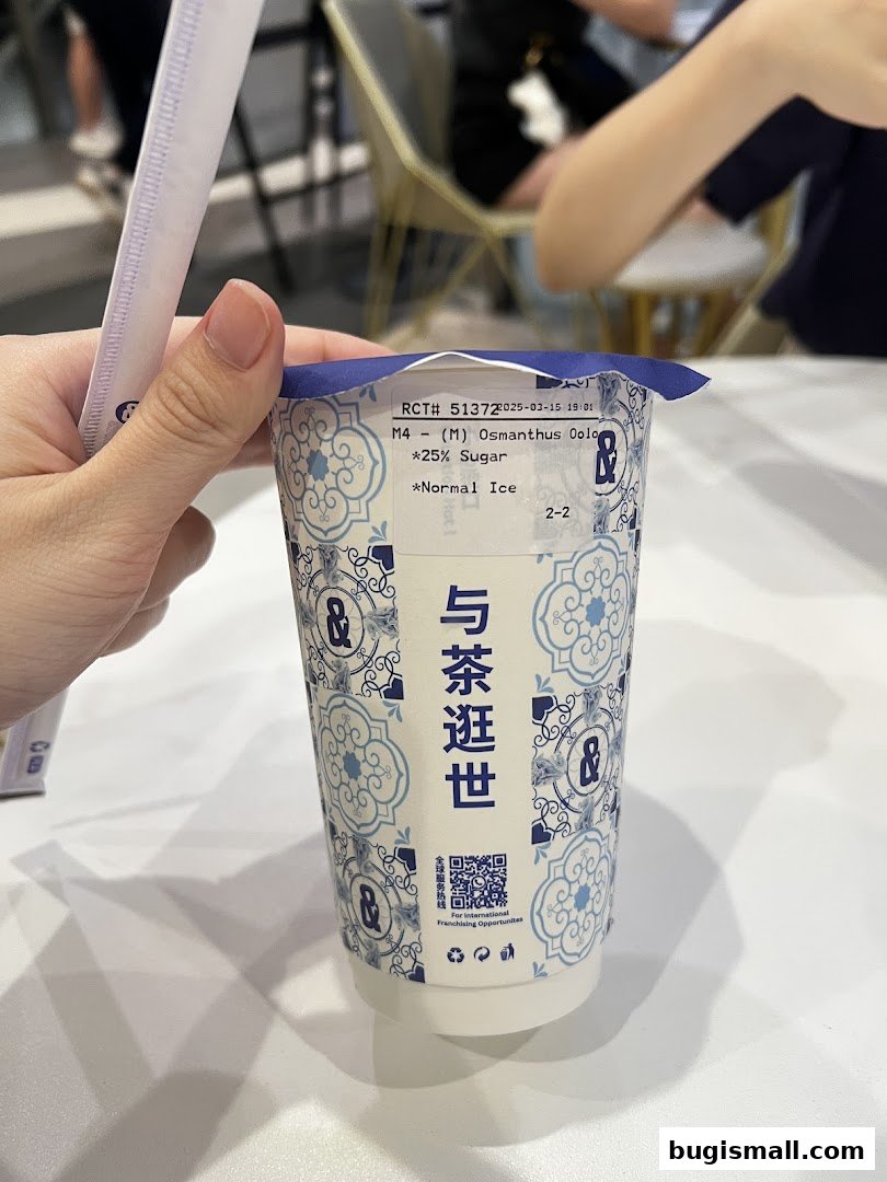 A hand holds a cup of Osmanthus Oolong tea with 25% sugar and normal ice.