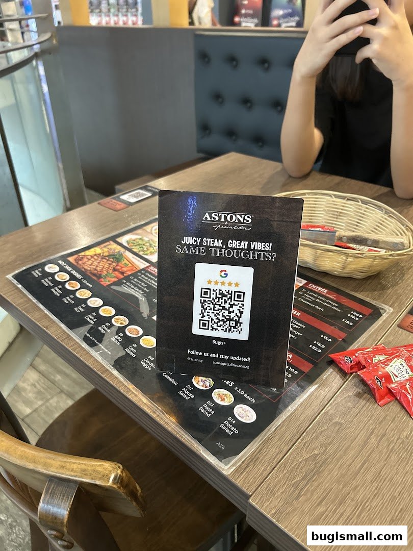 A table at ASTONS restaurant with a menu, QR code, and condiments.