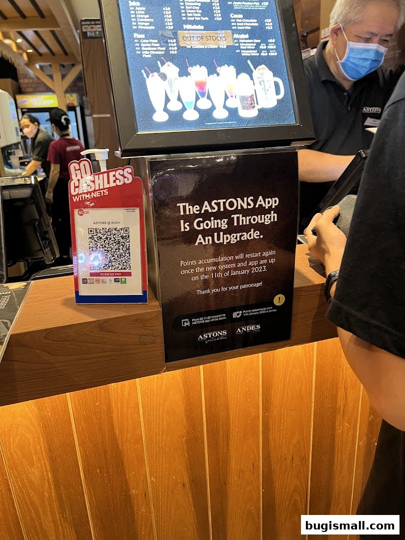 A counter at ASTONS with a QR code for cashless payment and an announcement about app upgrade.
