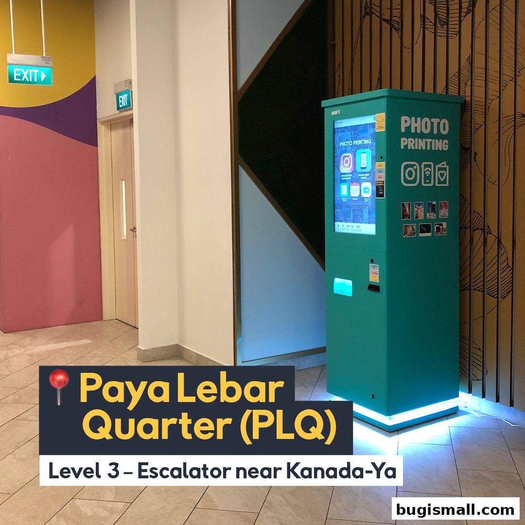 A teal photo printing machine is located in a mall hallway with colorful walls and exit signs.