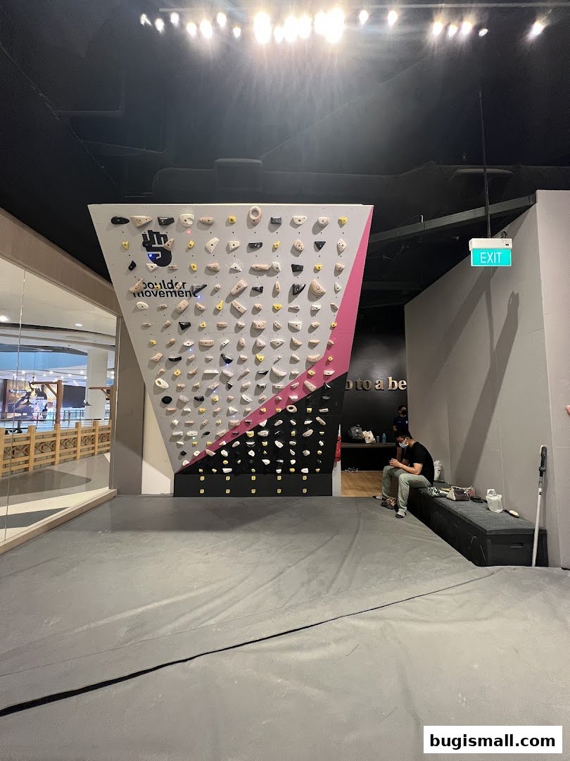 A bouldering gym with a climbing wall and a person sitting on a bench.