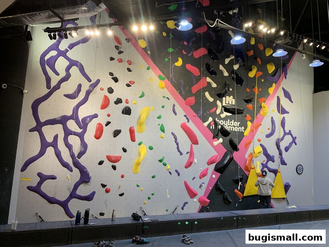 A bouldering gym with colorful climbing holds on a large wall and a person climbing.