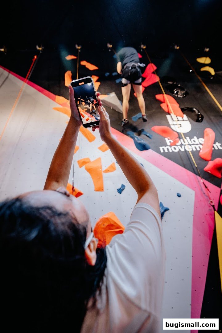 A person films a climber on a colorful bouldering wall at Boulder Movement.