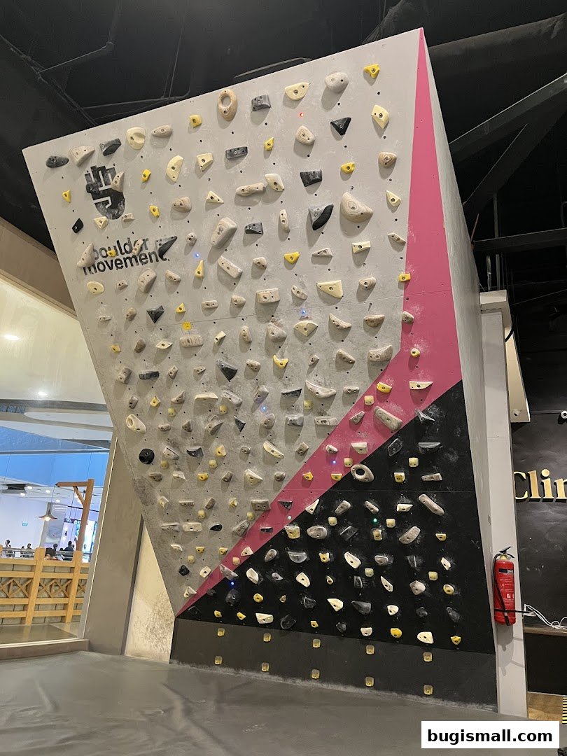 A large, colorful bouldering wall with numerous climbing holds and a fire extinguisher on the side.
