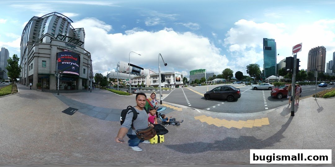 A family poses for a selfie in front of a modern building with a large digital advertisement.