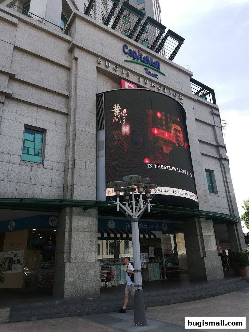 Exterior view of CapitaMall Bugis Junction with a large digital screen and shops below.
