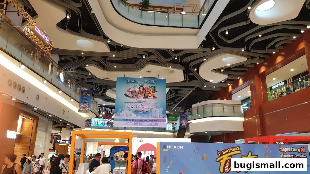 Interior view of a bustling shopping mall with various shops and promotional banners.