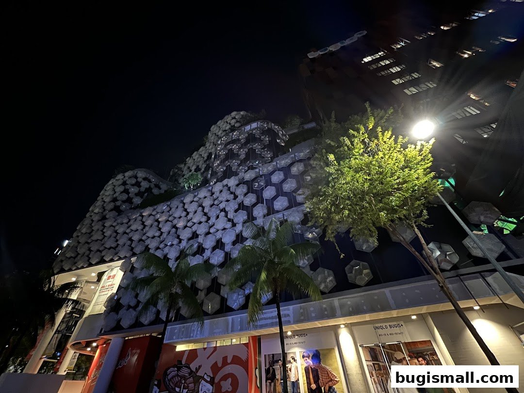 A nighttime view of a modern building with unique hexagonal facade and illuminated shop fronts.