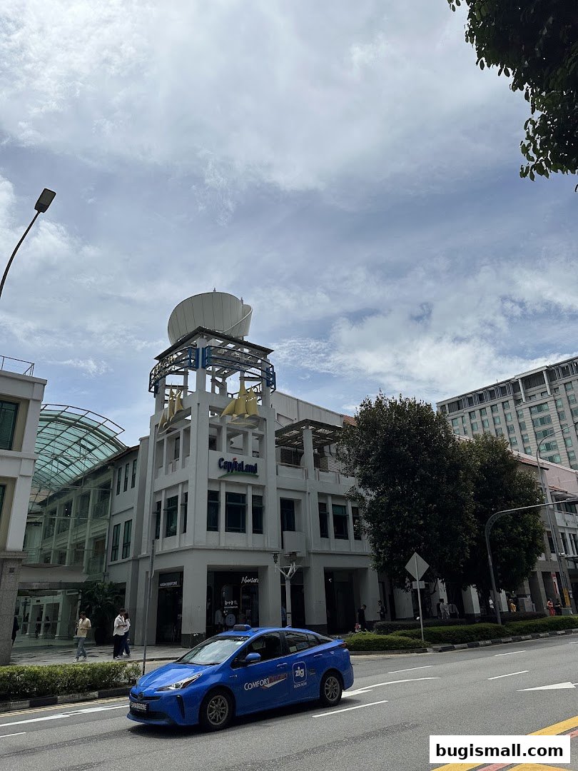 A blue taxi drives past a building with 'CapitaLand' signage and a distinctive rooftop structure.