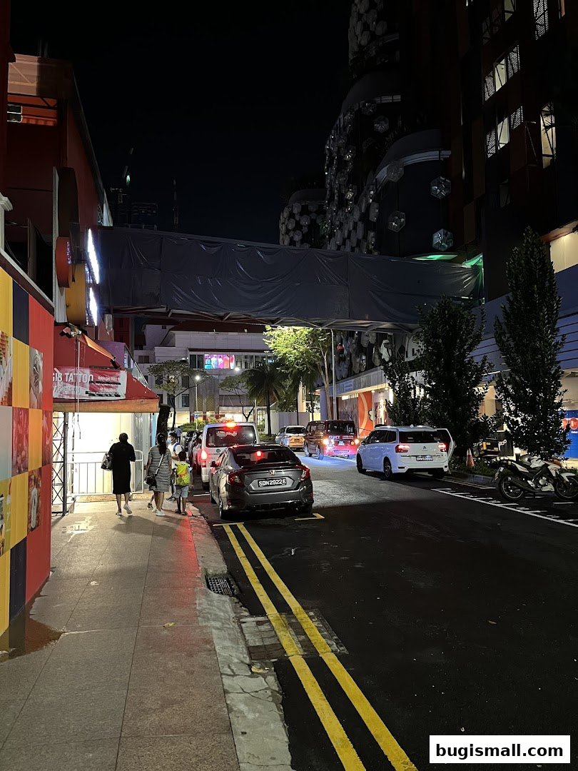 A street scene at night with cars, pedestrians, and illuminated buildings.
