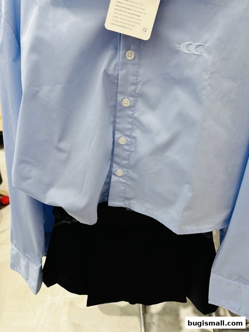 A light blue collared shirt with white buttons and a black skirt.