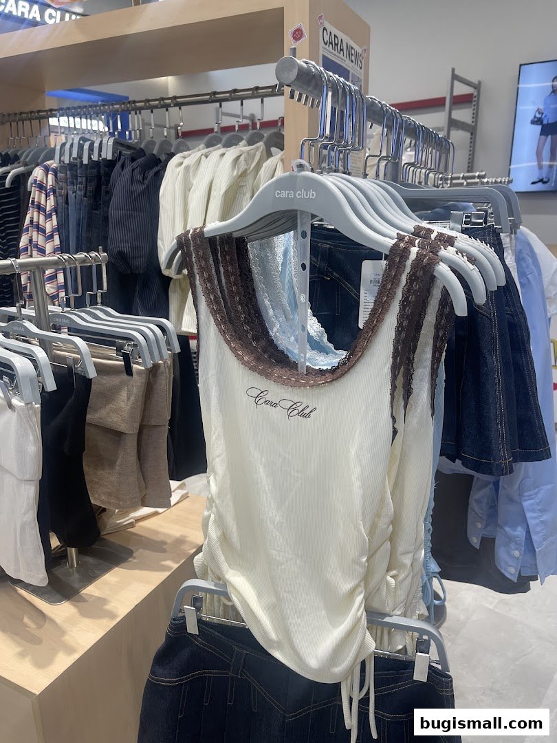 A display of trendy women's clothing, featuring a white ruched tank top with lace trim.