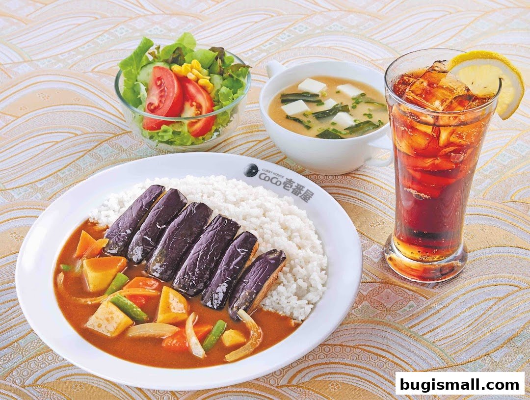 A delicious meal featuring Japanese curry with eggplant, rice, miso soup, salad, and a drink.