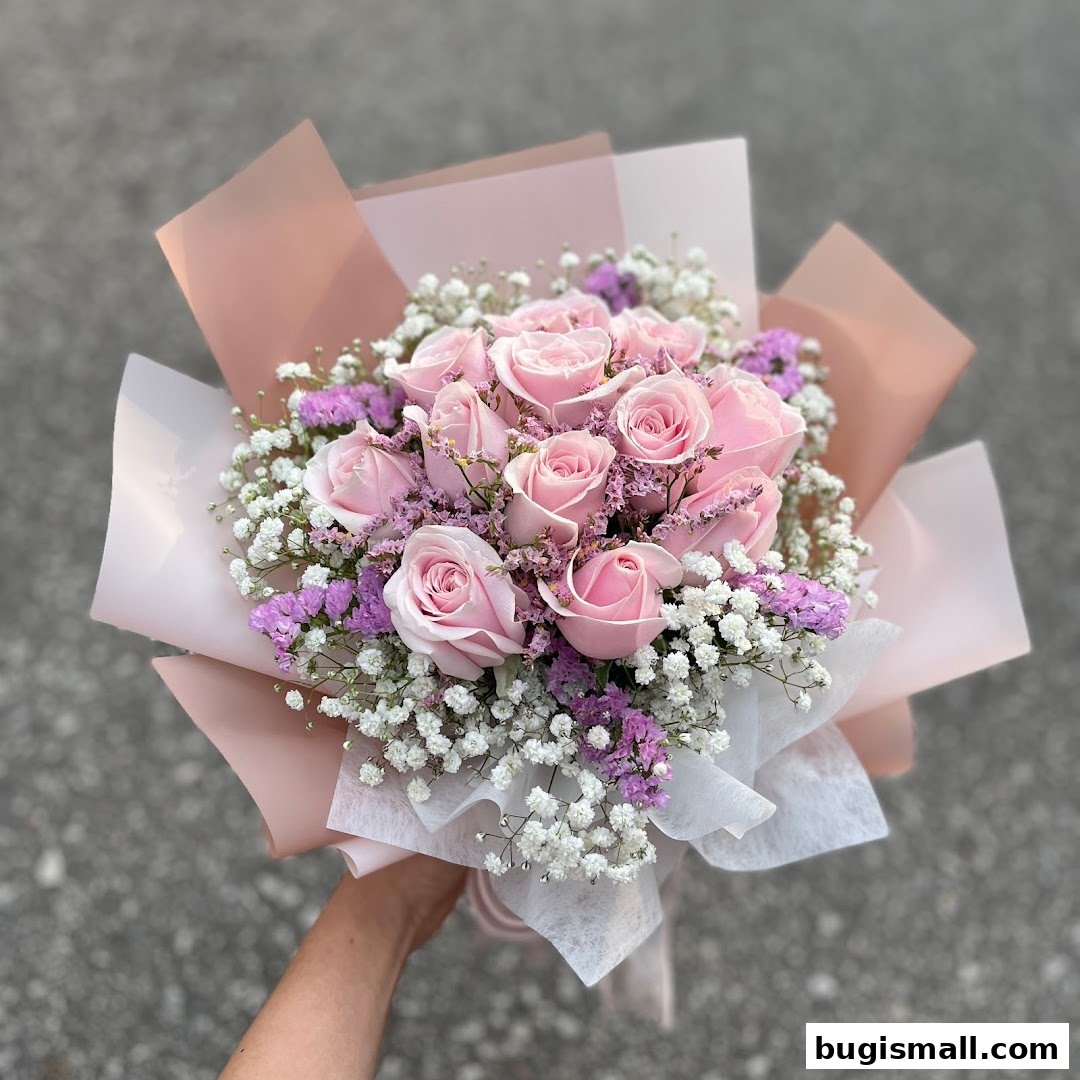 A hand holds a beautiful bouquet of pink roses with baby's breath and purple filler flowers.