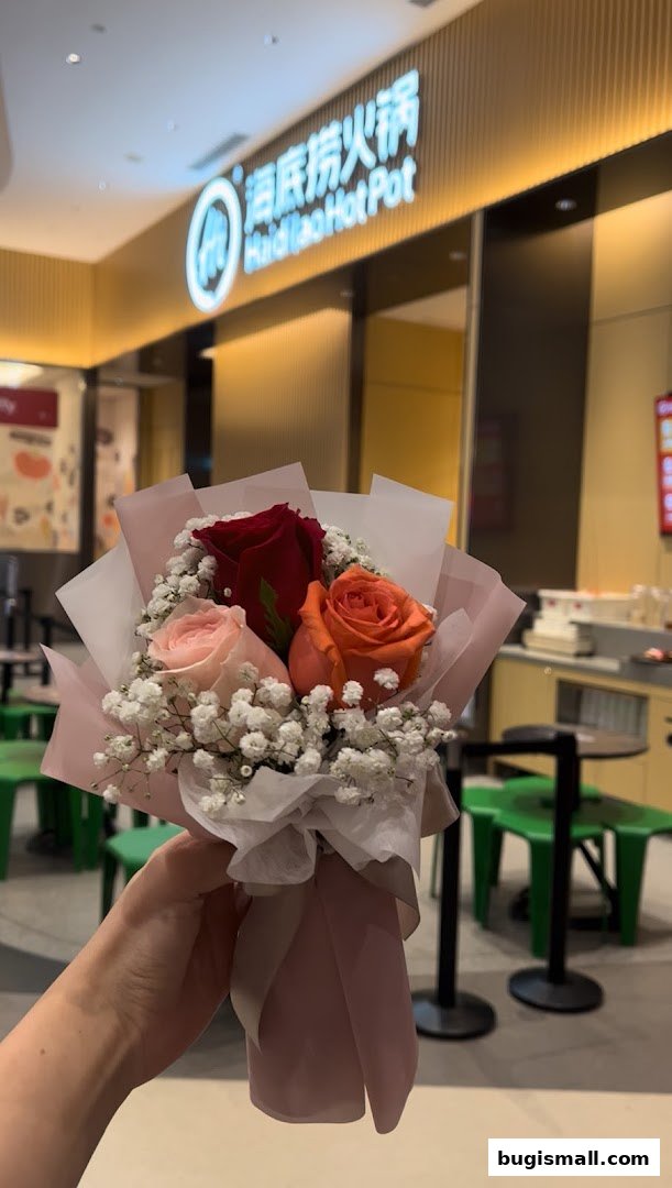 A hand holds a bouquet of roses in front of a Haidilao Hot Pot restaurant.