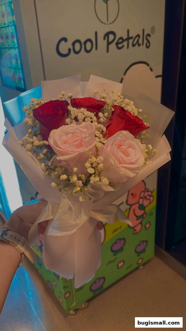 A hand holds a bouquet of red and pink roses with baby's breath, with the shop name 'Cool Petals' visible.