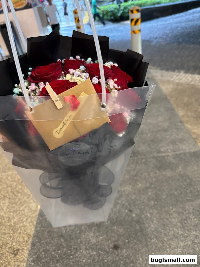 A bouquet of red roses with baby's breath in a clear bag with the shop's logo.