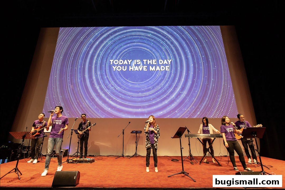 A band performs on stage with a large screen displaying lyrics and a circular pattern.