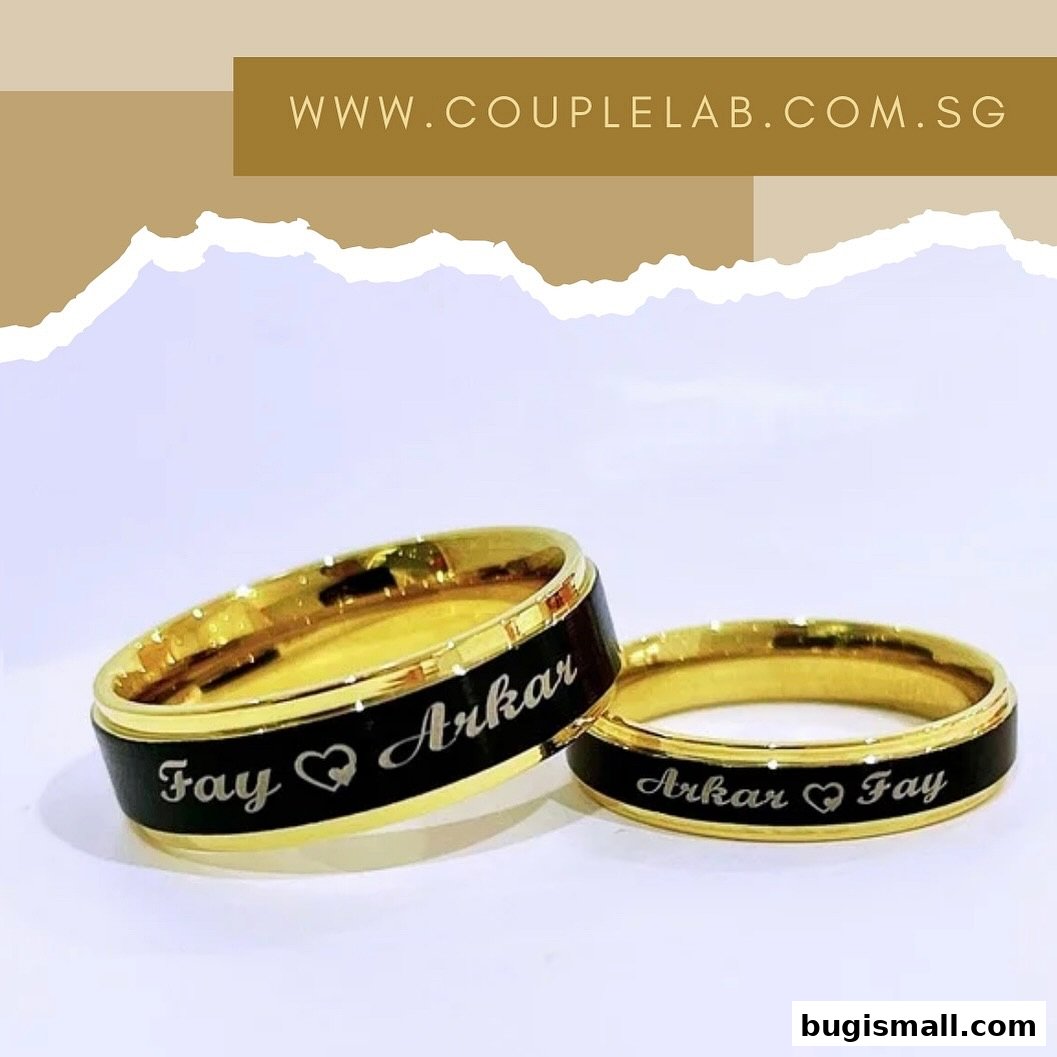 Two gold rings with black bands engraved with names and a heart symbol.