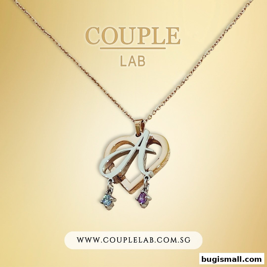 A rose gold necklace with a heart pendant featuring the letter 'A' and two dangling gemstones.