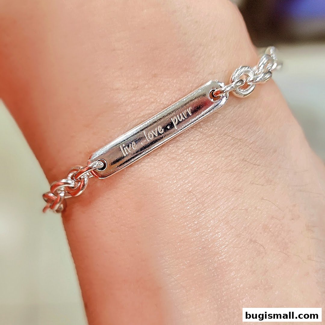 A close-up shot of a silver bracelet with the engraving 'live love purr' on a wrist.