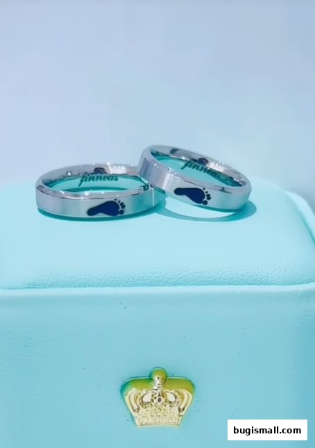 Two silver rings with blue footprint engravings and personalized text.