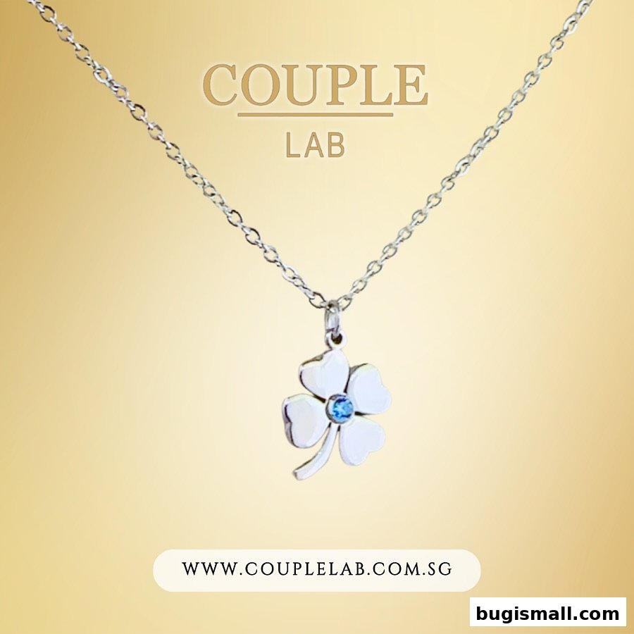 A silver necklace with a four-leaf clover pendant featuring a blue gemstone.