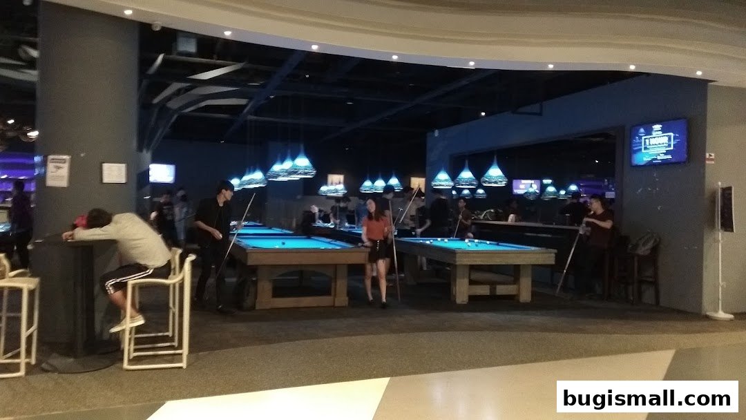 People playing pool in a dimly lit entertainment venue with blue lighting.