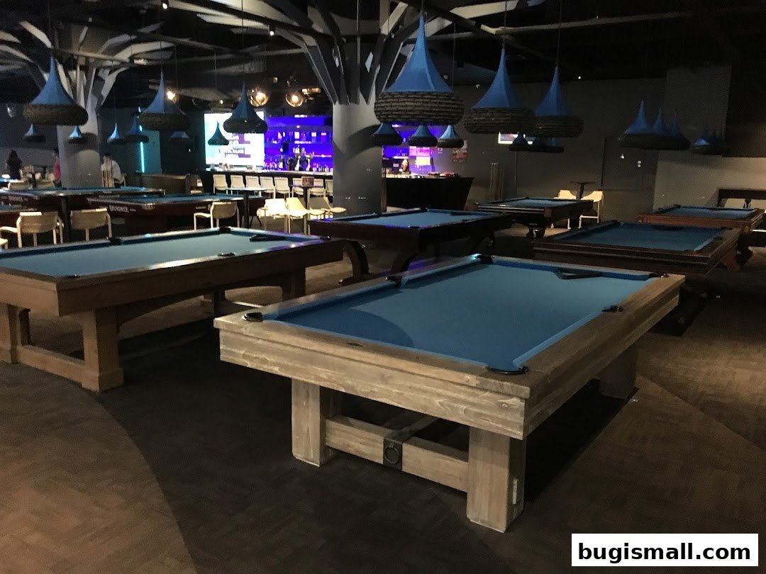 Interior of a modern billiards hall with multiple pool tables and a bar in the background.