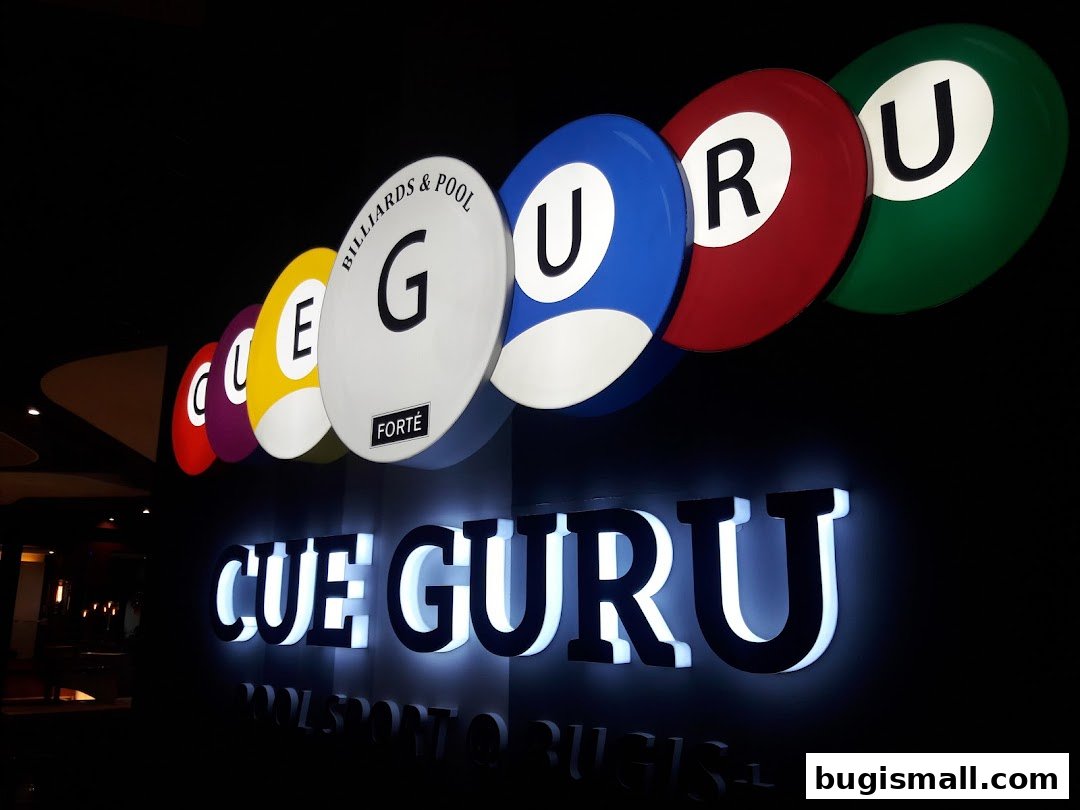 The illuminated sign for Cue Guru, a billiards and pool establishment, featuring colorful pool ball designs.