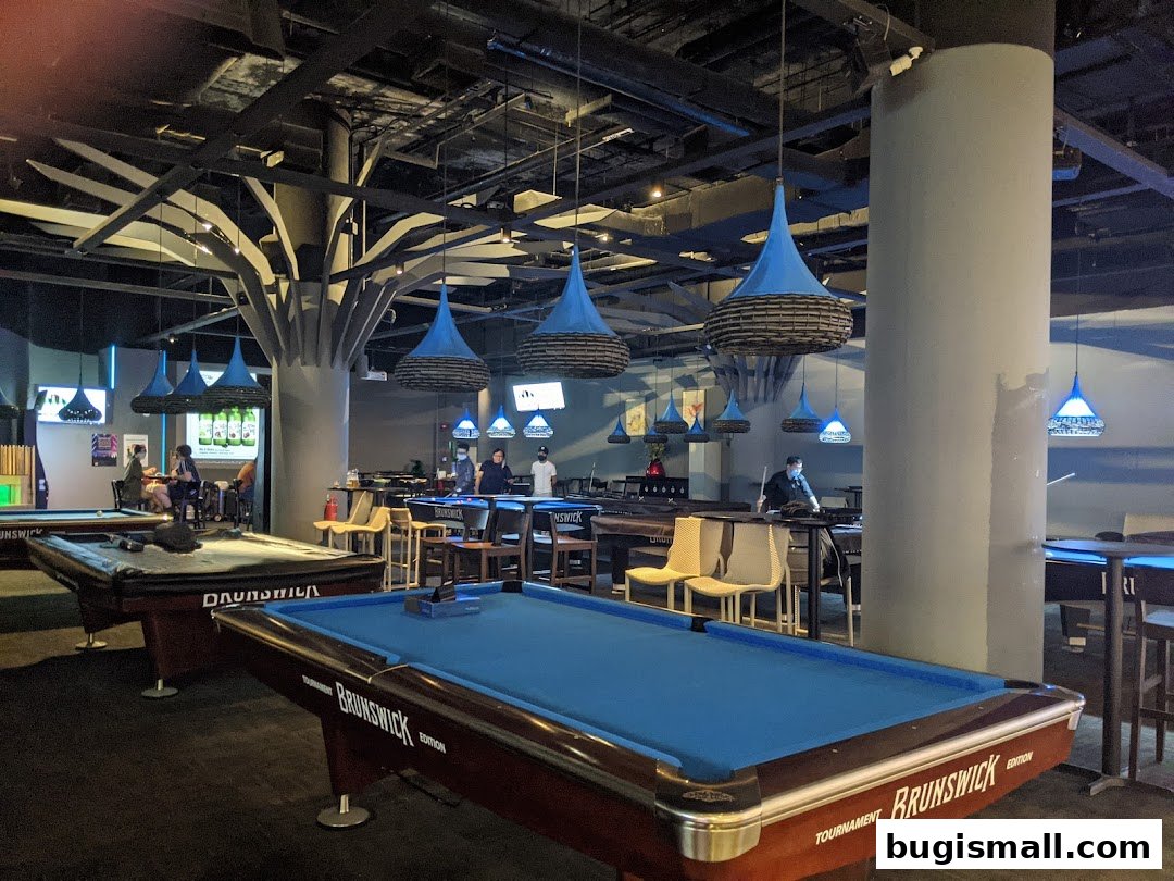 Interior of a modern billiard hall with multiple pool tables and stylish blue pendant lighting.