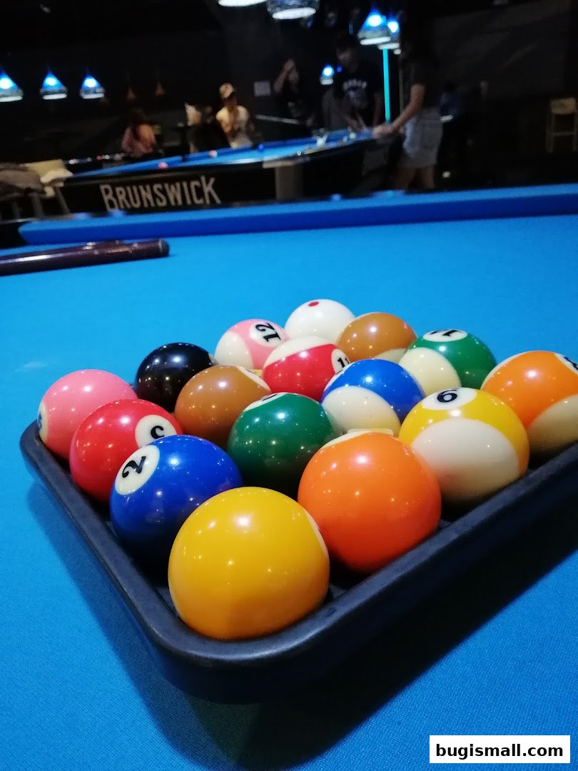 A rack of billiard balls on a blue pool table with people playing in the background.