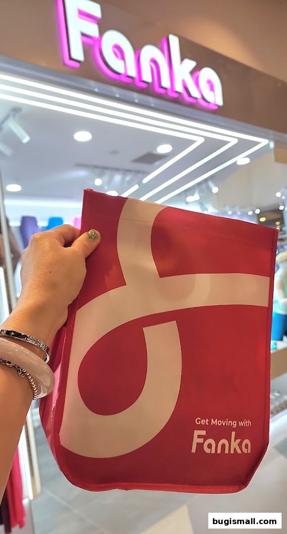 A hand holds a red Fanka shopping bag in front of the Fanka Singapore Bugis store.