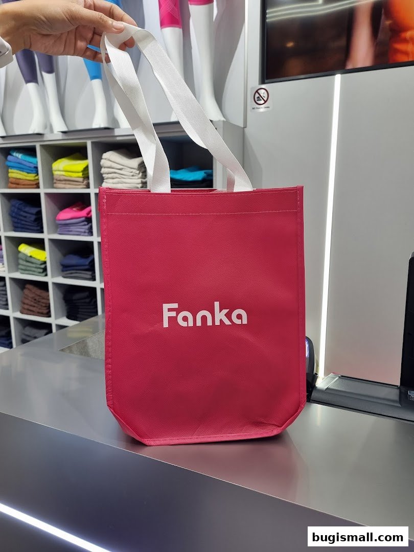 A hand holds a pink Fanka branded shopping bag in front of a store display.