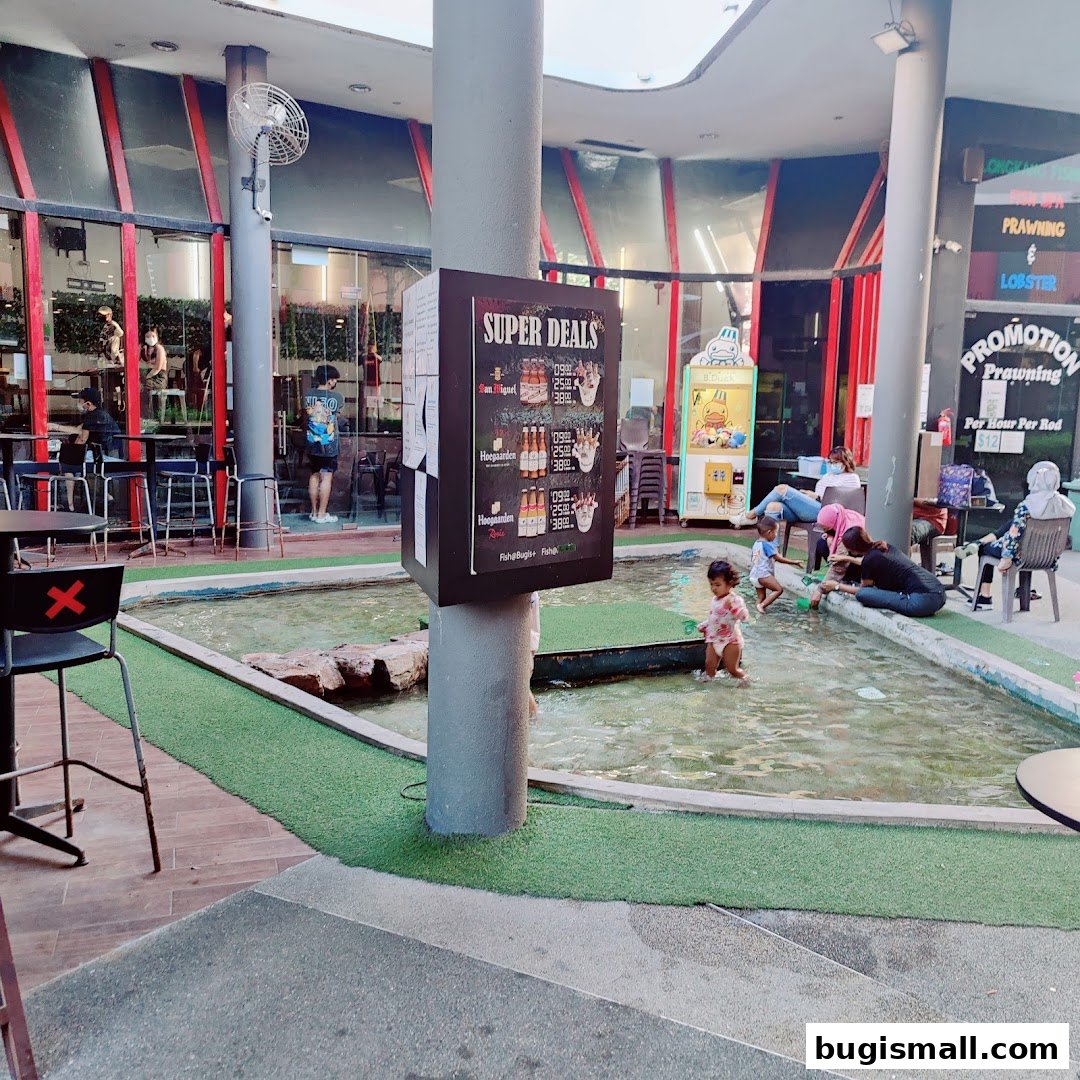 A family enjoys a shallow water play area outside a restaurant with a 'Super Deals' sign.