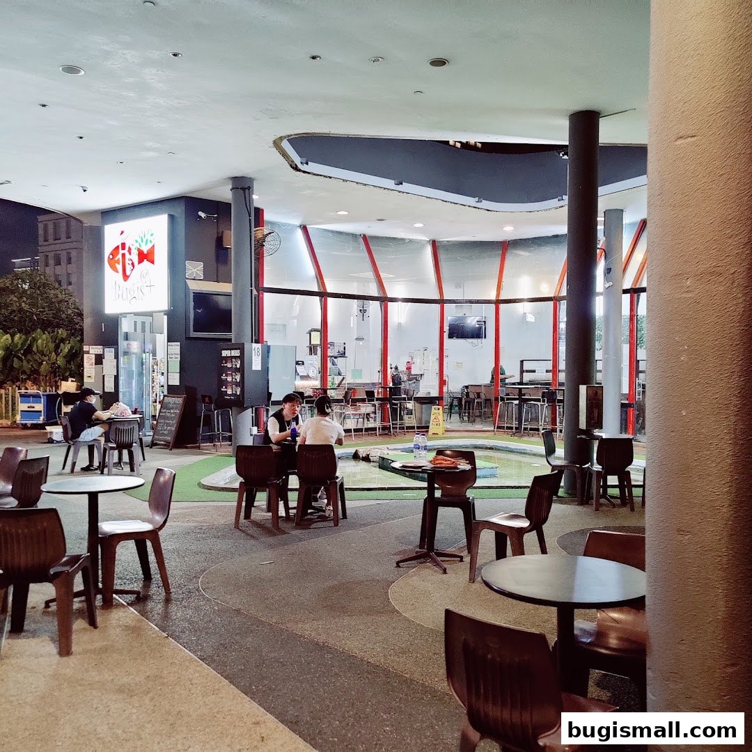 People dining at tables outside a restaurant with a modern, curved glass facade.