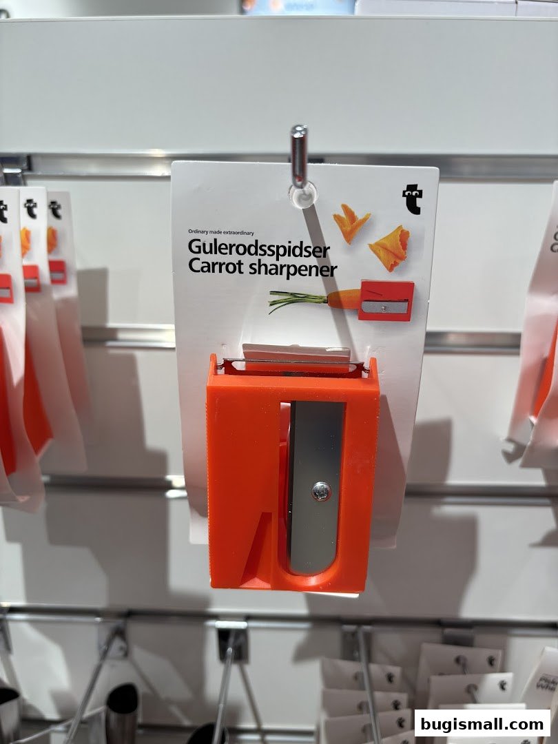 A bright orange carrot-shaped pencil sharpener is displayed on a white card.