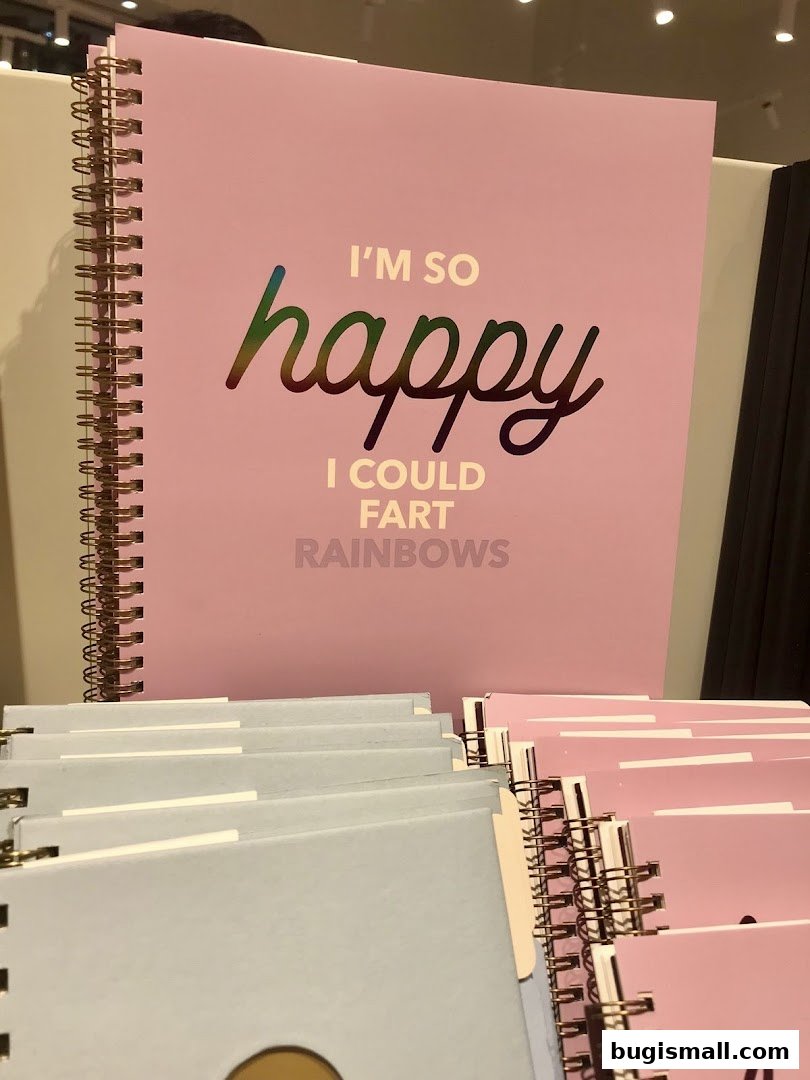 A close-up of pink notebooks with a humorous "happy" quote and a stack of light blue notebooks.
