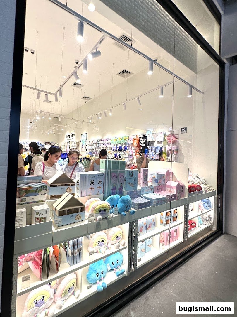 View of a Flying Tiger Copenhagen shop interior through a large glass window, showcasing colorful merchandise.