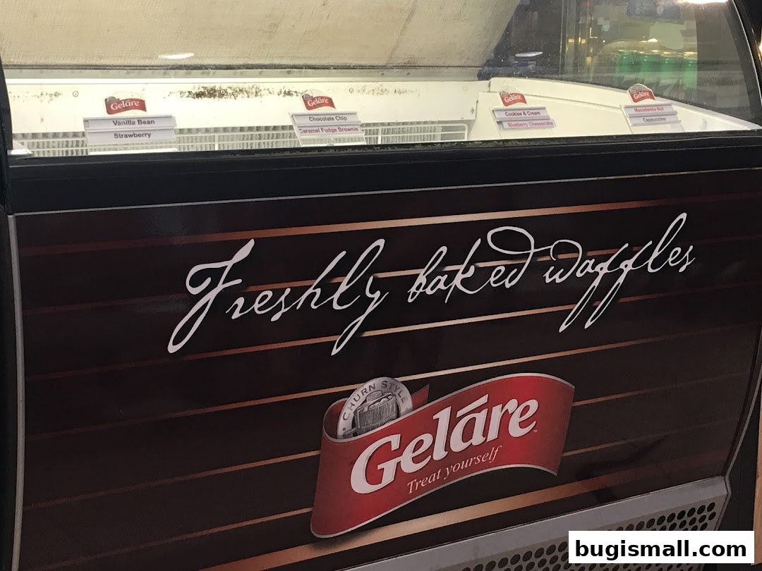 A Geláre ice cream display case featuring various flavors and promoting freshly baked waffles.