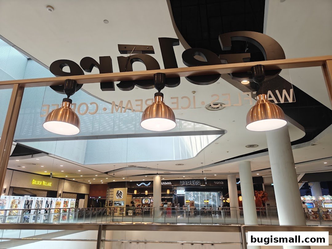 Interior view of a shopping mall with a Geláre shop sign and hanging lights.